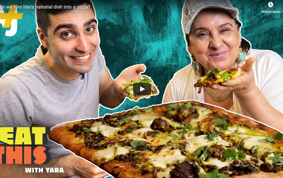 Screenshot of young man and older woman showing us a slice of pizza. Whole pizza in front.